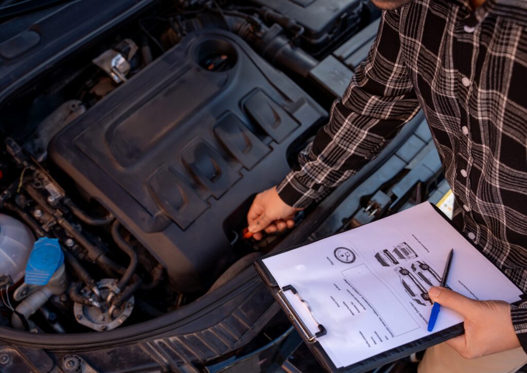 Mechanic inspecting a car engine while holding a car maintenance checklist on a clipboard for routine servicing.