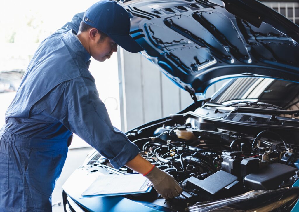 Mechanic inspecting a car engine with a clipboard, demonstrating what is a tune-up for vehicle maintenance.